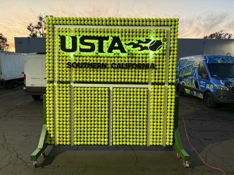 Custom step-and-repeat wall built from thousands of tennis balls with a cut-out USTA Southern California logo