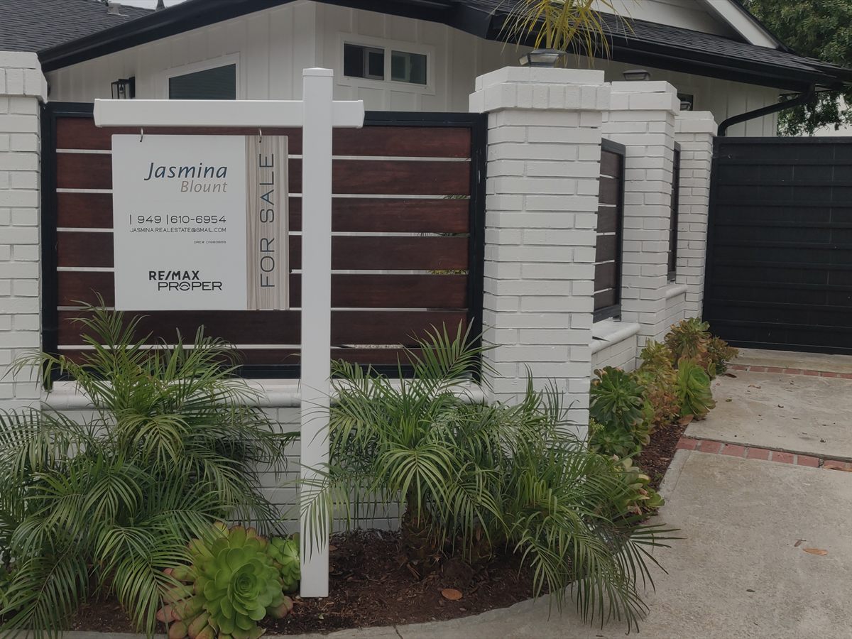 White post-and-panel real-estate sign with a For Sale rider outside a modern home